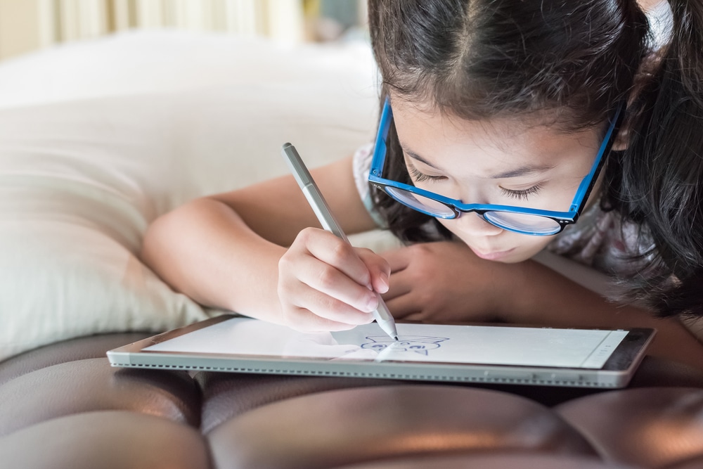 Asian girl kid in glasses drawing on a tablet