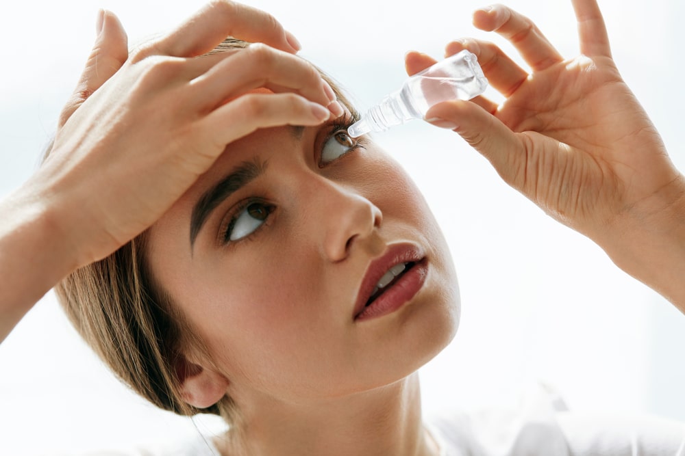 a woman putting eye drops in here eyes - one of the proper ways to clean your eyes.