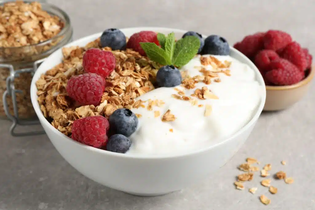 A bowl of yogurt topped with granola, raspberries, and blueberries, promoting a balanced, nutritious breakfast.
